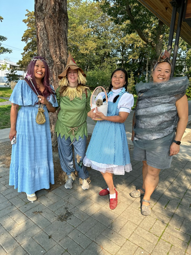 Four friends dressed as Glinda, Scarecrow, Dorothy, and a Tornado by a tree