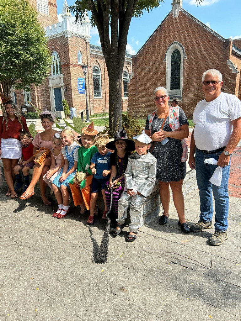 Group of kids in Oz costumes — Dorothy, Scarecrow, Wicked Witch, and Tin Man — by a church